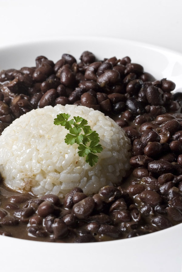 white rice accompained by black dry beans served in a plate with parsley decoration. vertical composition